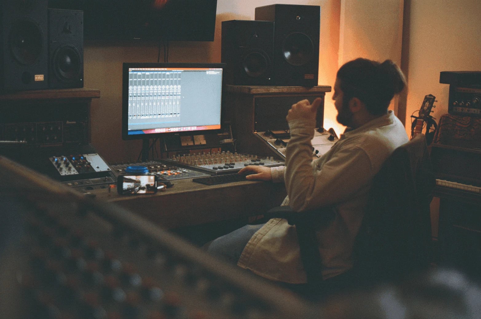 Rami seated at the mixing desk in a warmly lit recording studio, with speakers and a computer session in front of him.