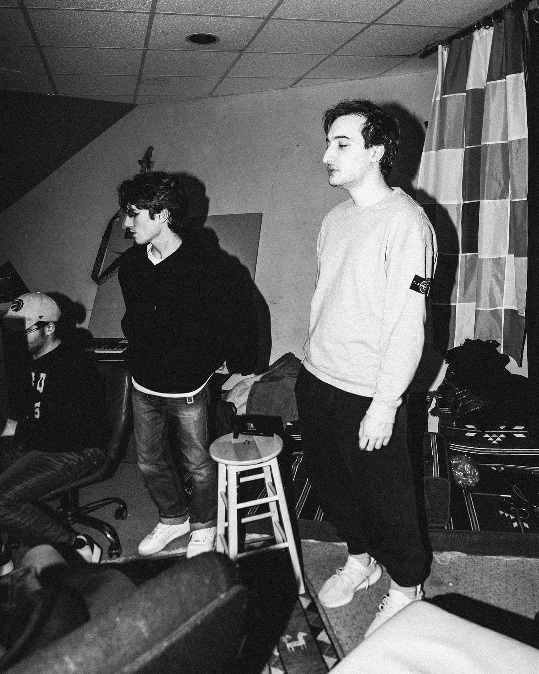 Black-and-white photograph of musicians gathered beside a drum kit in a recording room.
