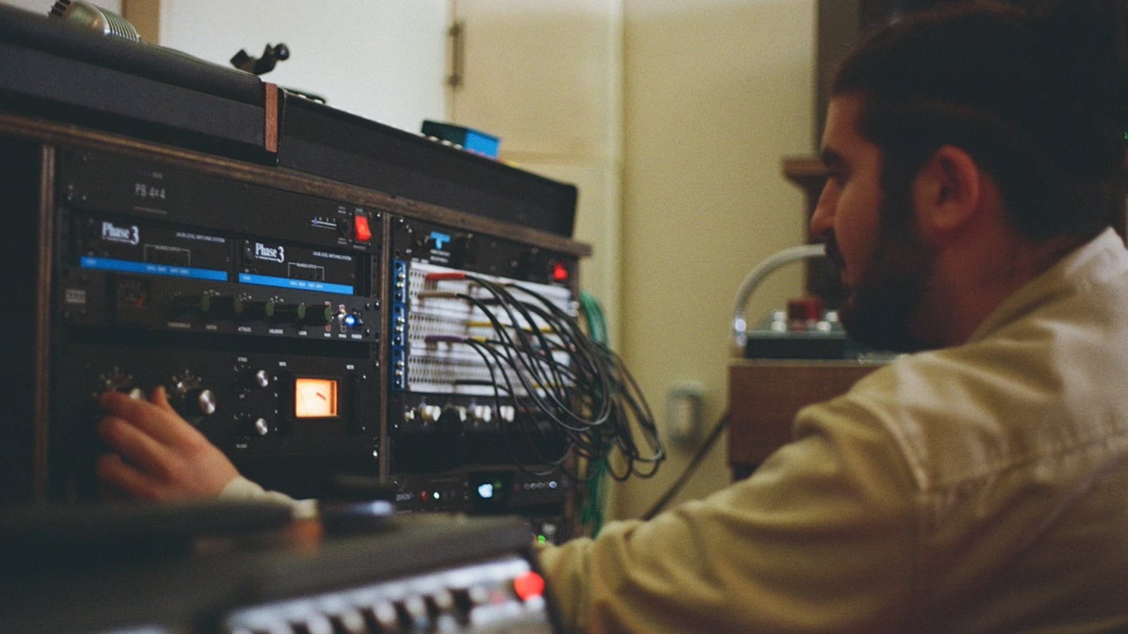 Rami adjusting vintage recording equipment beside a studio patchbay during the album sessions.